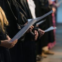 Choir singers holding musical score and singing on student graduation day in university, college diploma commencement